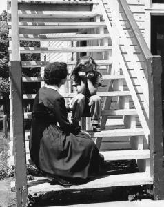Une fillette assise dans un escalier, tête penchée vers l’avant, coudes sur les genoux et mains devant les yeux. Devant elle, une femme est assise plus bas, regard tourné vers l’enfant et main posée sur les genoux de la fillette.