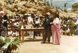 Photo prise dans un camp de réfugiés. Il y a une foule d'adultes et d'enfants à l'arrière-plan et, devant, une table avec quelques personnes debout, dont une femme avec un porte-voix