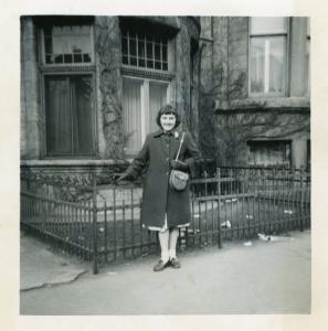 Photo en noir et blanc d’une jeune femme prenant la pose debout sur le trottoir devant la maison familiale.