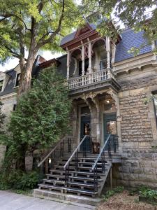 Deux arbres et une maison de deux étages en pierres grises sur une rue.