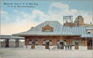 Carte postale colorée d’une petite gare de brique avec une dizaine de personnes devant, dont des enfants.