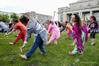 Photo couleur d’une foule colorée qui danse sur la pelouse devant une ancienne gare.