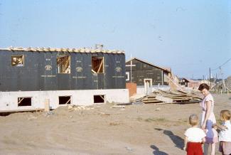 Des maisons en construction dans un nouveau quartier résidentiel. Il n’y a pas d’arbres ni de pelouse. Une mère et ses deux jeunes enfants sont dans le coin inférieur droit de la photo. 