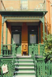 Photographie couleur de la façade d’un duplex avec un balcon peint en vert et deux portes au-dessus de chacune desquelles se trouve une plaque d’adresse bleu et blanc.