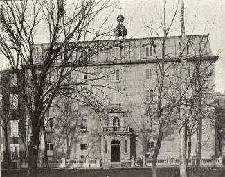 Photographie en noir et blanc représentant un édifice de cinq étages, avec un toit mansardé et un clocheton.