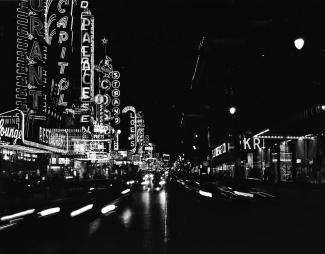 Photo en noir et blanc montrant la rue Sainte-Catherine de nuit avec les enseignes néon.