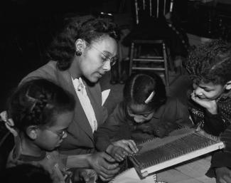 Une jeune femme montre à des enfants comment utiliser un petit métier à tisser.