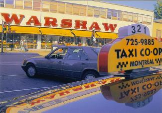 Photo couleur montrant en gros plan un lanternon de la compagnie Taxi CO-OP dans le stationnement d’un magasin Warshaw qu’on voit en arrière-plan.