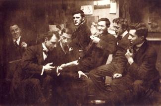 Groupe de sept hommes assis fumant la pipe et discutant