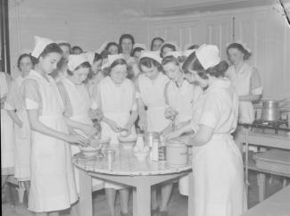 Jeunes femmes en uniforme préparant une recette autour d'une table.