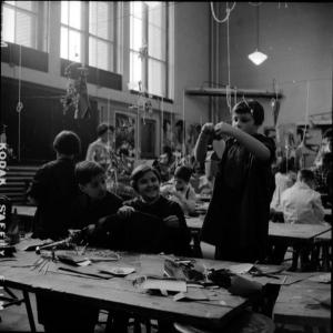 Photographie en noir et blanc montrant une salle de classe remplie d’enfants travaillant sur des projets artistiques.