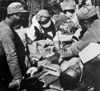 Photo en noir et blanc montrant Bethune opérant un blessé, entouré d'hommes l'assistant.