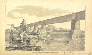 Vue générale du pont Victoria depuis les rives de Montréal. On aperçoit le pont à une voie ferrée, tel que construit initialement, sous forme d'un long tube reposant sur les piles de maçonnerie. Il y a quelques embarcations de petite taille en avant-plan.