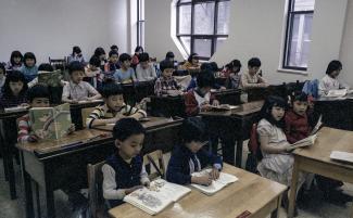 Jeunes élèves d’origine chinoise assis à leur pupitre dans une grande salle de classe.