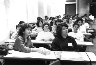 Fotografia a preto e branco de um grupo de mulheres sentadas e atentas numa sala de conferências.