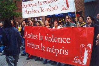 Une quinzaine de personnes se tiennent derrière deux  grandes bannières, l’une rouge, l’autre blanche. On peut y lire : « Arrêtez la violence, arrêtez le mépris, Stella »