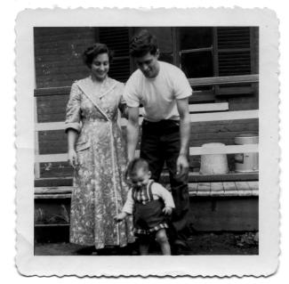 Photographie de deux parents souriant derrière leur jeune enfant.