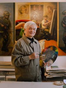 Colour photograph of an artist in his studio, holding a paintbrush and palette.