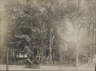 Photographie de la résidence clôturée et entourée d'arbres, ainsi que de la voiture en avant-plan.