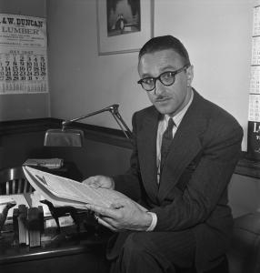 Photographie en noir et blanc d’un homme portant un complet-cravate et des lunettes à monture épaisse.