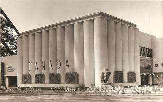 Photographie du bâtiment ayant abrité le pavillon du Canada, devant lequel il y a une statue de bison. On peut lire les inscriptions «  Forêts fourrures pêcheries » (à gauche) et « Mines agriculture » (à droite). 
