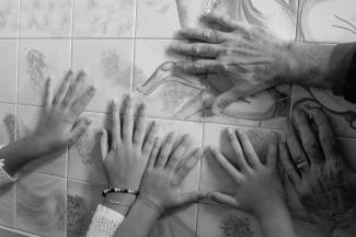 Photo en noir et blanc montrant les mains d’un grand-père et de deux de ses petits-enfants qui sont appuyées sur un mur en plan rapproché.