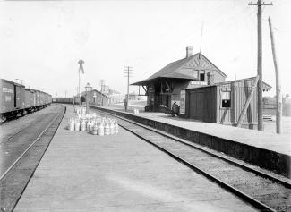Photo en noir et blanc d’une très petite gare bordée par deux voies ferrées.