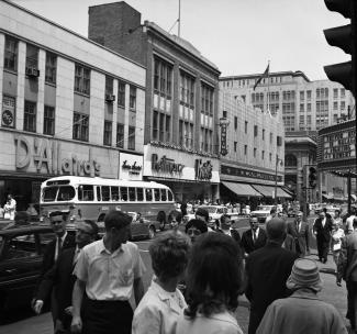 Vue sur les magasins de la rue Sainte-Catherine de jour, avec de nombreux passants et la circulation dans la rue. 