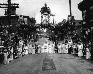 Réunies sous l’arche fleurie, des fillettes aux atours angéliques côtoient de jeunes garçons habillés en petit page pour la procession de la Fête-Dieu