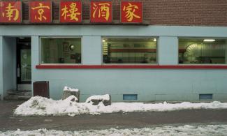 Photo couleur de l’extérieur du restaurant Ho Ho prise en hiver, la porte d’entrée se trouve à gauche et trois fenêtres donnent un aperçu de l’intérieur. 
