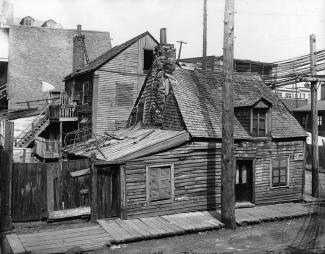 Photographie d'une maison en bois typique du quartier. On remarque que son toit s'affaisse au centre.