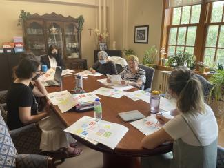 Sept femmes sont assises autour d’une grande table en réunion.