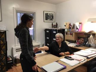 Deux femmes souriantes dans un bureau, l'une assise derrière le bureau, l'autre debout devant