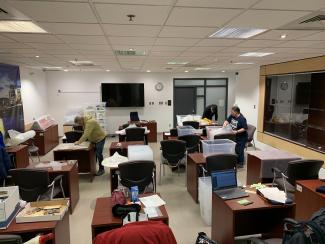 Photographie en couleur montrant trois personnes en train d’emballer des items dans une salle de classe.