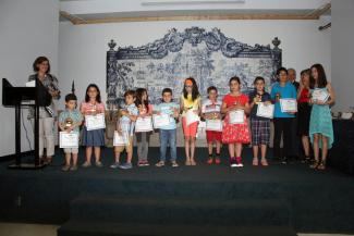 Des élèves sont debout sur une scène et tiennent des diplômes et trophée. Ils sont entourés de leurs enseignants.