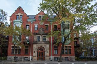 Photographie en couleurs d’un édifice à appartements de style Queen Anne principalement construit de briques rouges. 