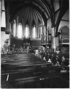 Intérieur d’une église avec des rangées de bancs à l’avant-plan. Au fond, au centre, le maître-autel est visible avec, à droite, un orgue. 