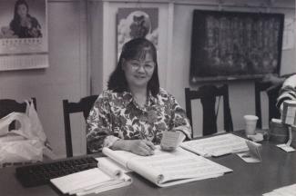 Une femme d’origine chinoise est assise derrière une table, des livres de compte ouverts devant elle.