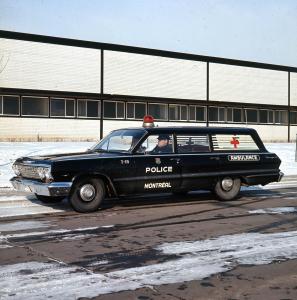 Photographie couleur d’une ambulance noire. Sur la porte du côté conducteur, les mots police et Montréal sont écrits en majuscules. Du même côté, à l’arrière, il y a le mot ambulance. Un gyrophare rouge est visible sur le toit de la voiture.  