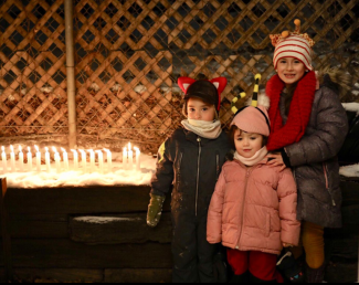 Trois enfants habillés chaudement avec une rangée de bougies allumées à leur gauche