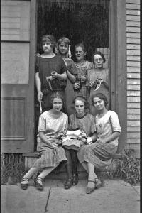 Sept femmes, dont trois assises et quatre debout derrière elles, dans l’entrée d’un édifice. 