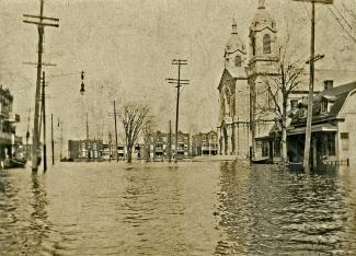 Une place inondée, entourée de maisons et d’une église. 
