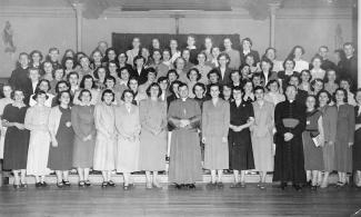 De nombreuses jeunes femmes et quelques prêtres posent pour une photo. Ils sont debout et organisés en quatre rangées.