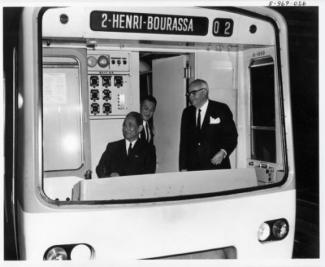 Deux ministres chinois et Lucien L'allier souriant dans un wagon de métro affichant « 2 - Henri-Bourassa »