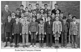 Photo en noir et blanc montrant les garçons d’une classe de 5e année posant devant les portes de l’école à l’extérieur. 
