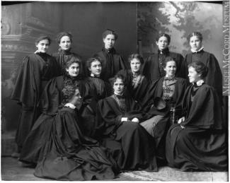 Photographie en noir et blanc montrant un groupe de jeunes femmes portant des toges de remise des diplômes noires.