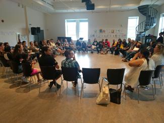 Une trentaine de personnes sont assises sur des chaises en cercle dans une grande salle.