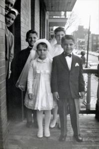 Quatre enfants habillés pour leur communion sur un balcon au 3e étage d’un triplex. Les parents sont à la porte. 