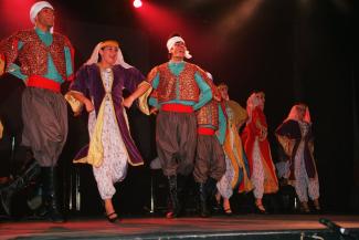 Sept artistes vêtus d’habits traditionnels se trouvent sur une scène.