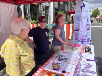 Photo couleur montrant trois femmes derrière un kiosque sur rue lors d’un événement.